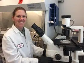 Julie Wilhelmy in a lab, sitting at a microscope. 