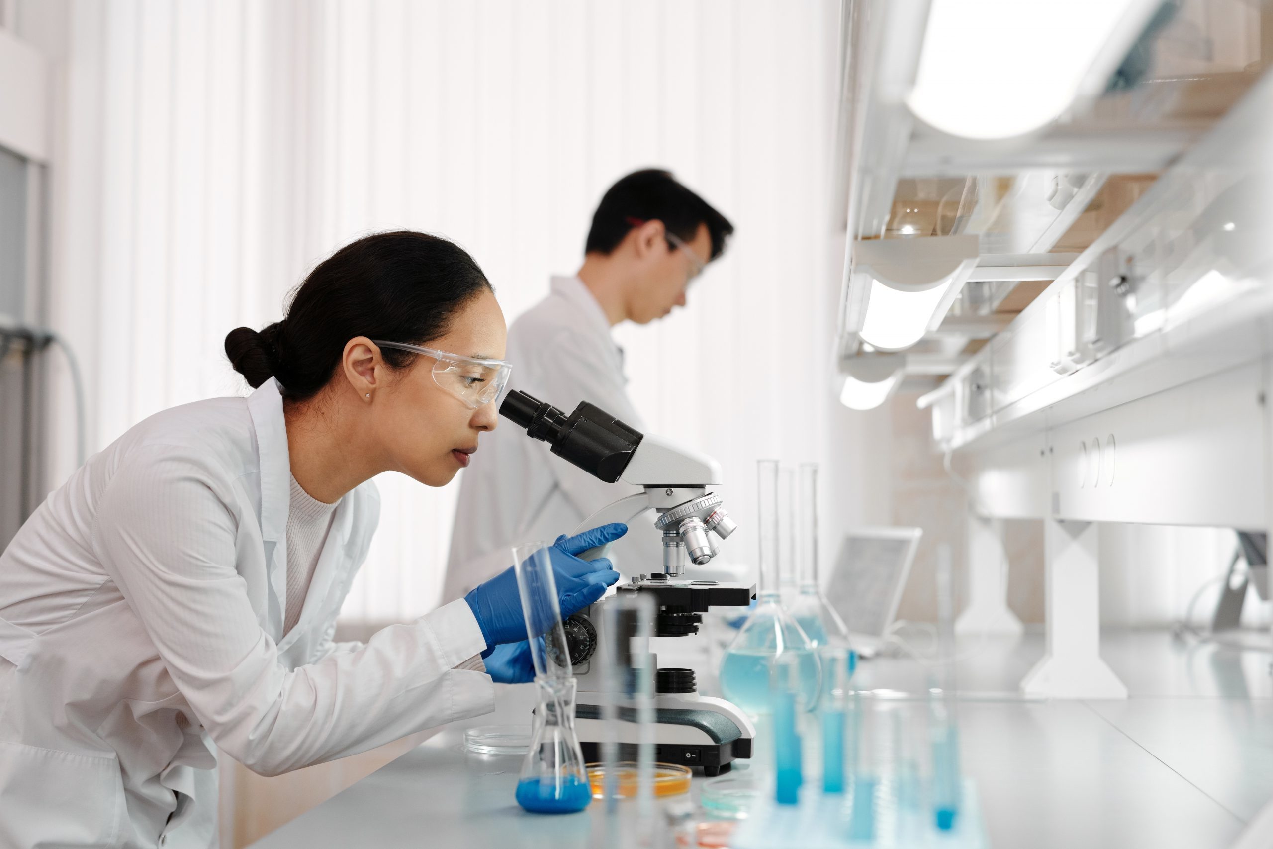 Woman researcher looking through a microscope. Male researcher in the background