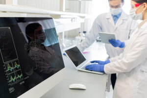 Two researchers in a lab near equipment. Each looks at data on a screen. 