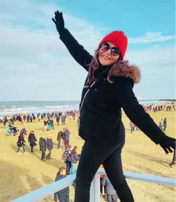 Faten debout sur une structure en bois sur une plage, vêtue d'une veste et d'un bonnet. À droite, une citation d'Faten : « J'ai trouvé le salut dans le pouvoir de mon esprit. Aujourd'hui, je reconnais que cette maladie a dégradé la qualité de ma vie, mais en retour, elle a renforcé mon amour de la vie.